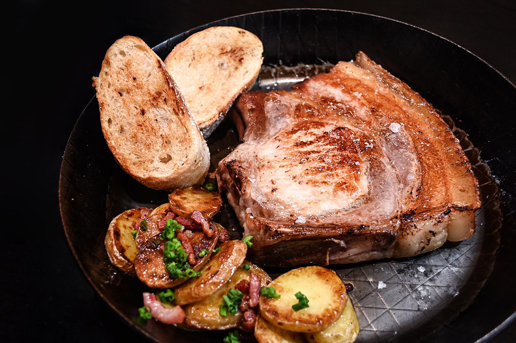 Dry Aged Kotelett vom Aktivstall-Schwein fertiges Dry Aged Kotelett vom Aktivstall-Schwein mit Bratkartoffeln und Brot