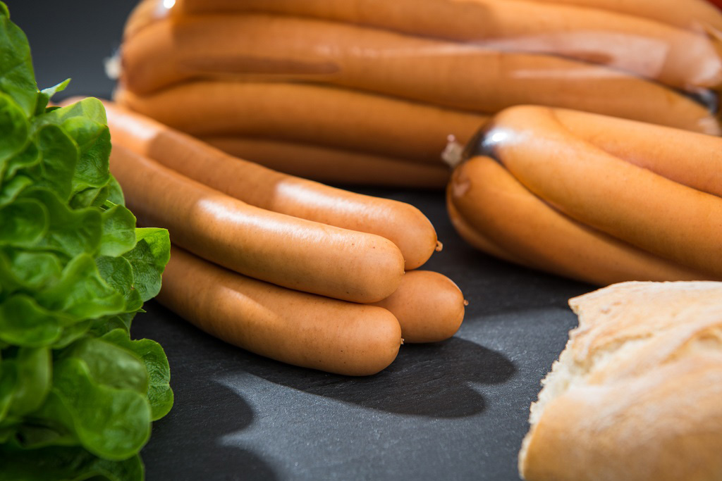 4 Wiener Würstchen, im Hintergrund weitere Packungen und Dekoration