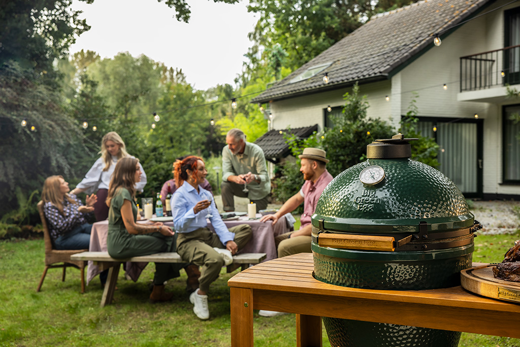 Big Green Egg Grill reunde sitzen zusammen im Garten, rechts steht ein Grill
