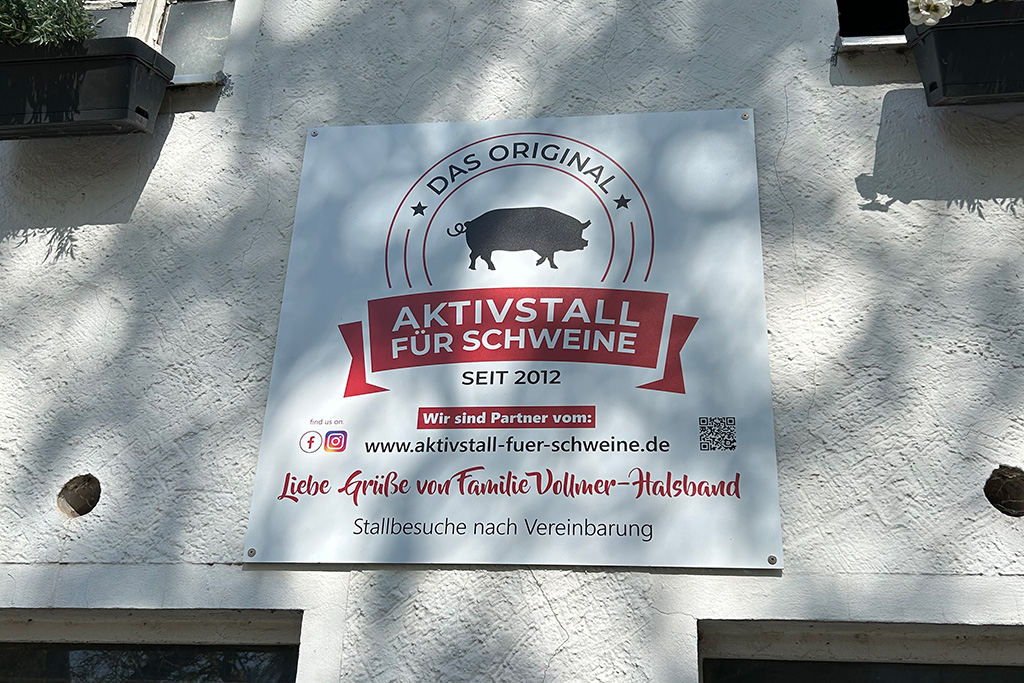 Schild Aktivstall für Schweine an Stall-Außenwand