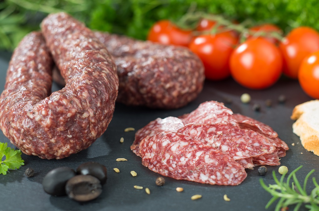 Salami aufgeschnitten und am Stück neben Dekoration wie Oliven und Tomaten